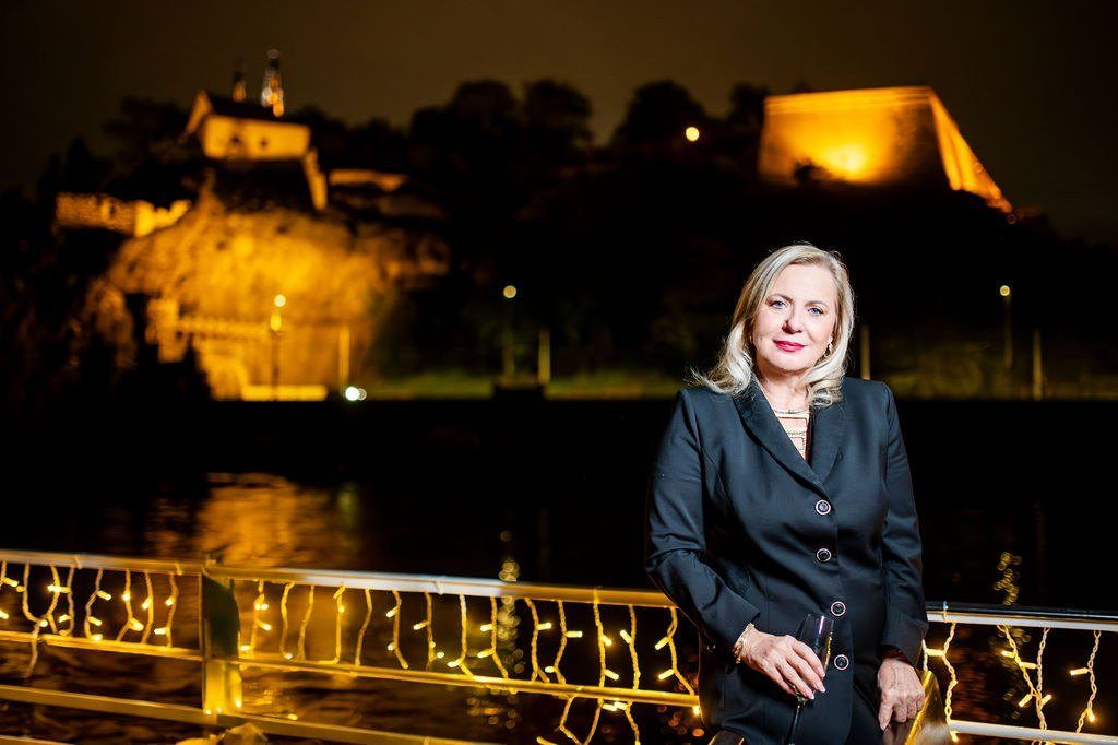 Eva Poláčková v noci u zábradlí se světelným řetězem, v pozadí nasvícený hrad